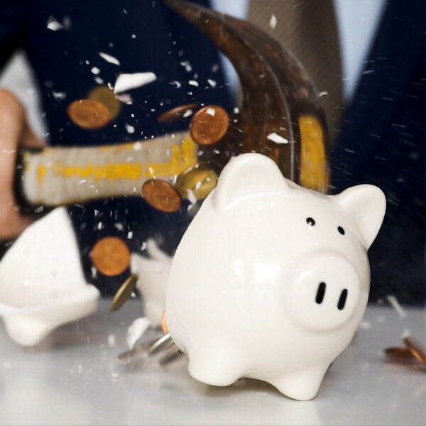 Close-up of businessman using a hammer to smash plenty of coins inside piggybank into pieces as he needs emergency money - using money in financial crisis concept. Close-up of businessman using a hammer to smash plenty of coins inside piggybank into pieces as he needs emergency money - using money in financial crisis concept