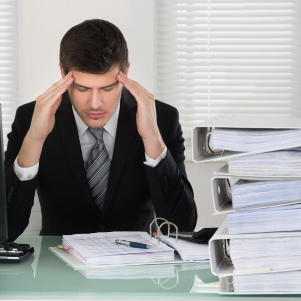 Businessman Suffering From Headache Businessman Suffering From Headache With Invoice On Desk